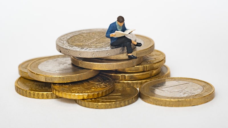 Miniature figure sitting on a stack of coins, representing building savings one small step at a time