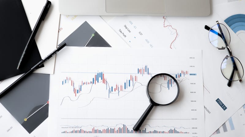 Investment charts and magnifying glass on a desk, representing the analysis needed to balance emergency savings and investing